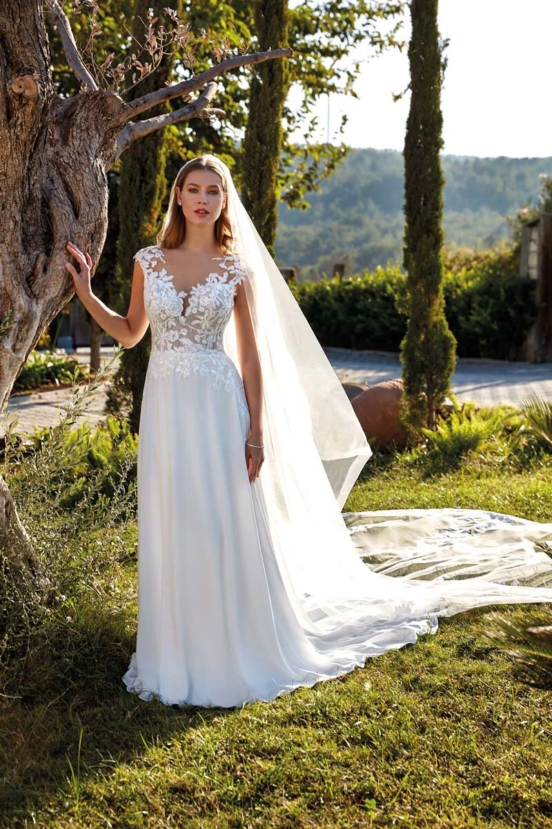 Sposa a figura intera con abito dalla linea scivolata e velo lungo in un giardino